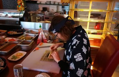 Gäste rollen Maki mit der Bambusmatte – praktische Übung im Kurs