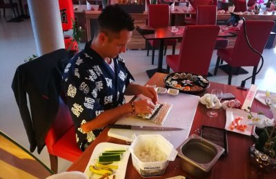 Teilnehmer beim Rollen von Maki – Sushi-Reis, Fisch und Gurke vorbereitet